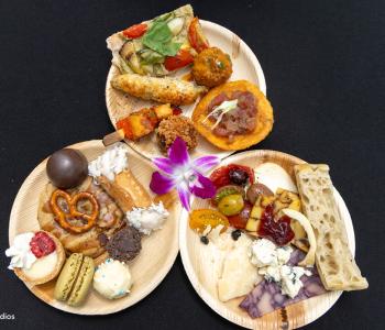 Three plates of food at the Presidential Farewell Reception at University at Buffalo's Center for the Arts. The top has a meatball, grilled wrapped asparagus, flatbread and other hors d'oeuvres. The bottom left has desserts, and bottom right has bread, cheeses and olives. Photo by Bellini Studios.