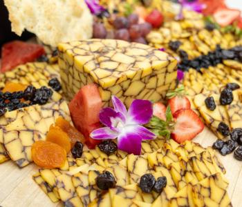 Close up of sliced cheese at the Presidential Farewell Reception at University at Buffalo's Center for the Arts. Apricots, raisins, strawberries and purple flowers also decorate the cutting board it is displayed on. Photo by Bellini Studios.